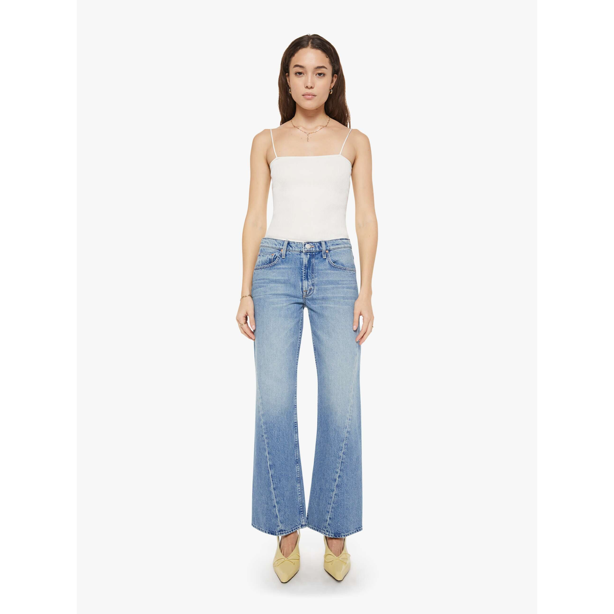 A model wearing a white spaghetti-strap camisole top and light blue wide-leg jeans with a subtle gradient wash, paired with beige pointed-toe heels, set against a plain light gray studio background.