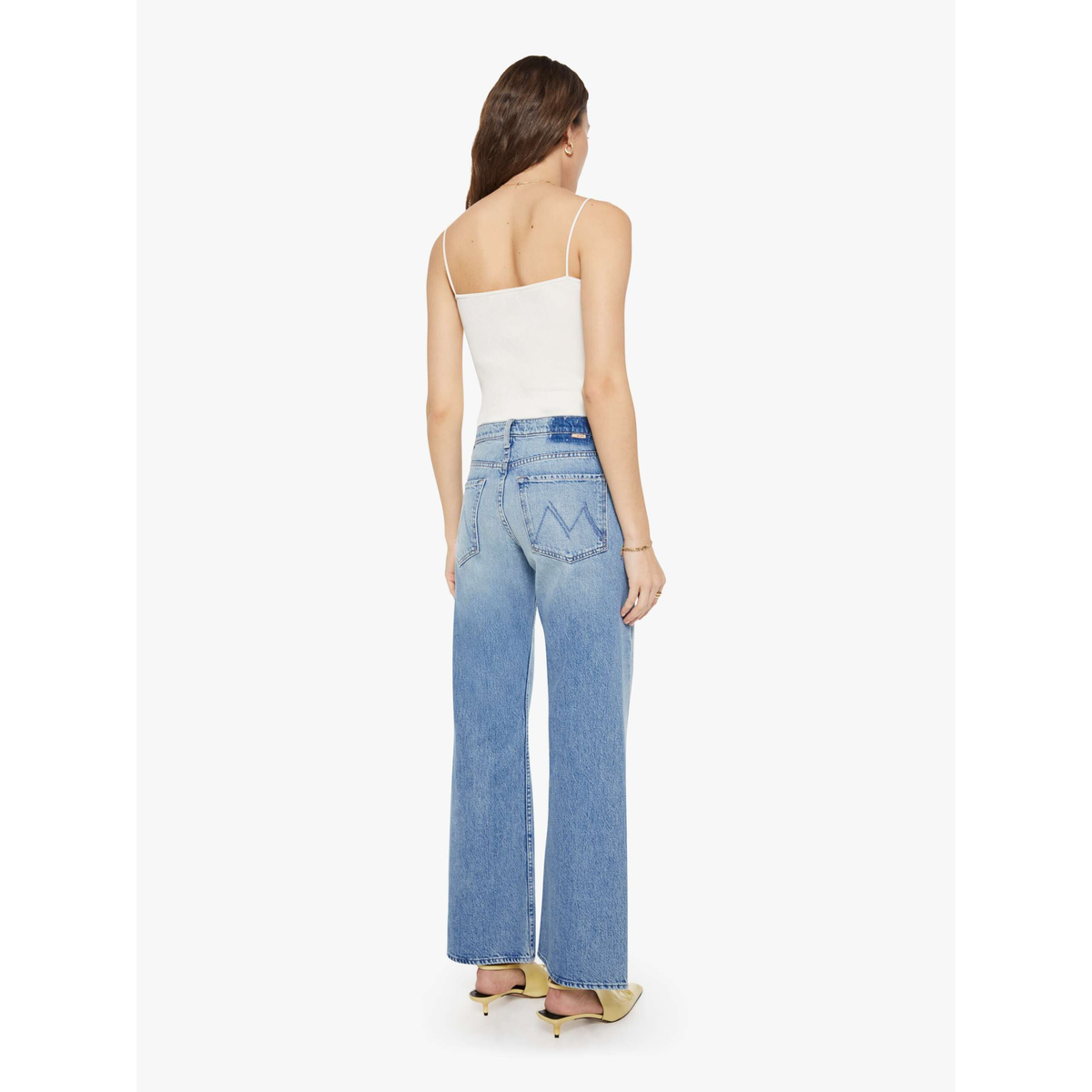 A woman shown from the back wearing light-wash wide-leg blue jeans, a white spaghetti-strap camisole, and beige high-heeled sandals against a plain light gray studio background.