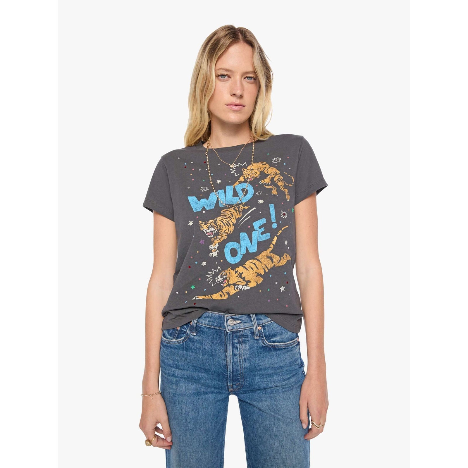 A woman modeling a dark gray graphic t-shirt with a tiger and the words 'WILD ONE!' in blue and orange, paired with blue jeans, against a light gray background.