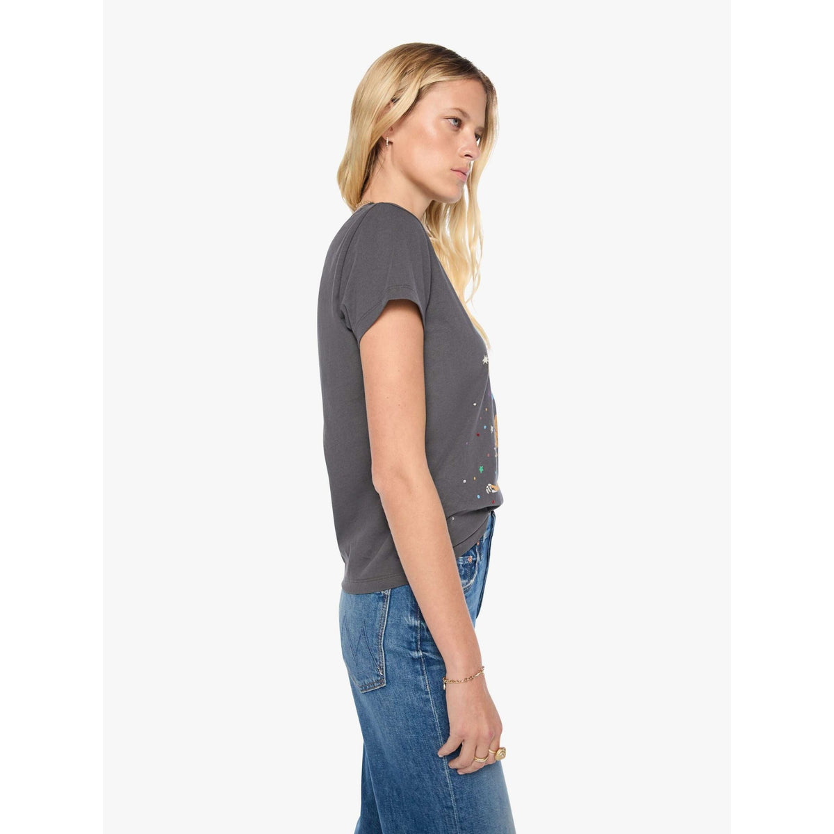 A woman shown in side profile wearing a dark gray short-sleeve t-shirt with colorful paint splatter details and blue jeans, set against a plain light gray background.