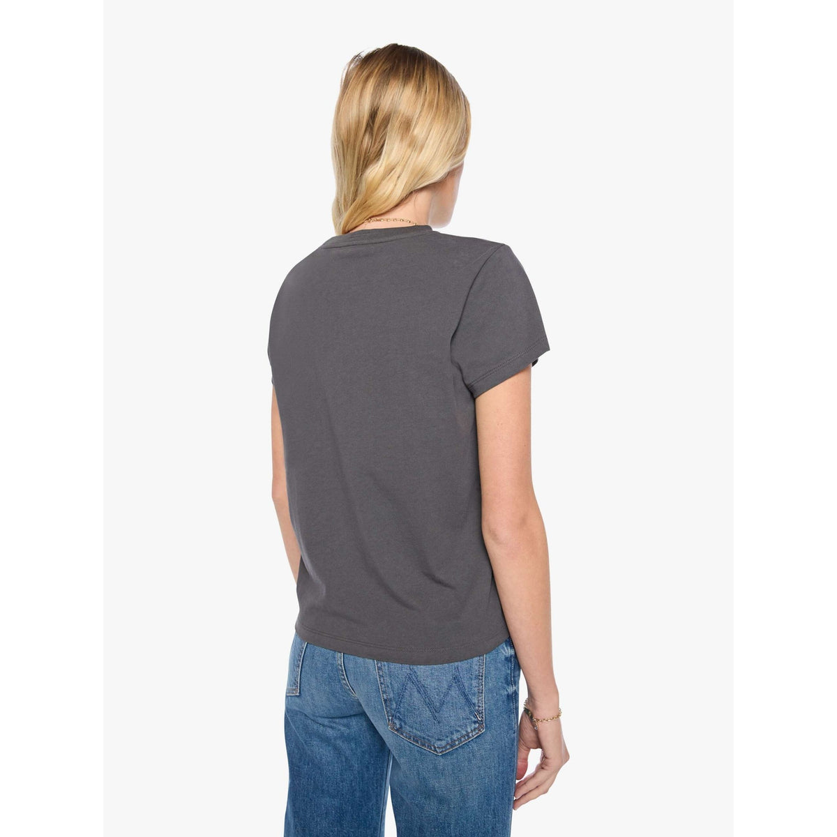 A woman viewed from the back wearing a dark charcoal gray short-sleeve t-shirt and blue jeans, standing against a plain white studio background.