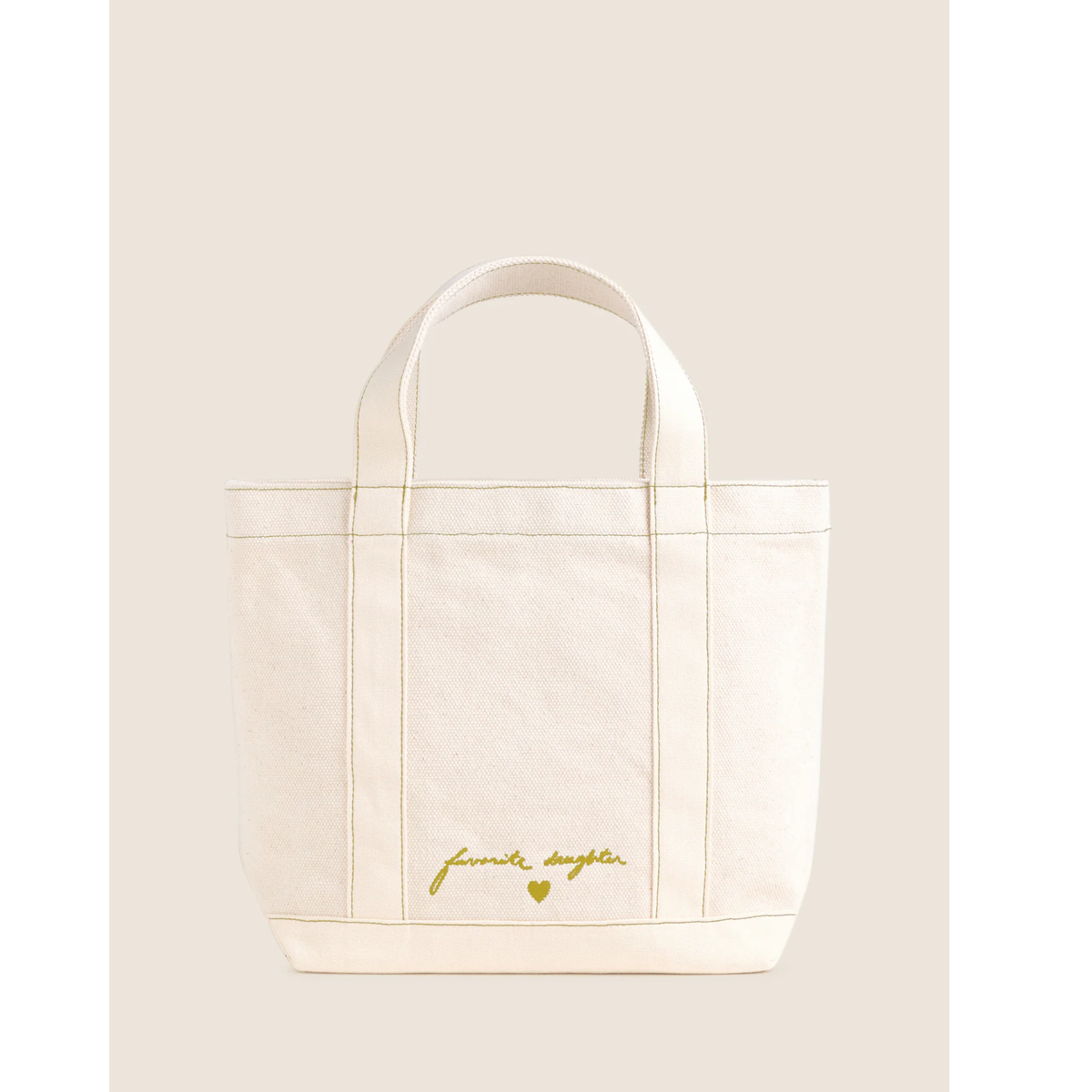An off-white canvas tote bag with gold foil script reading 'femme daguer' and a small gold heart on the front, set against a solid light beige background.