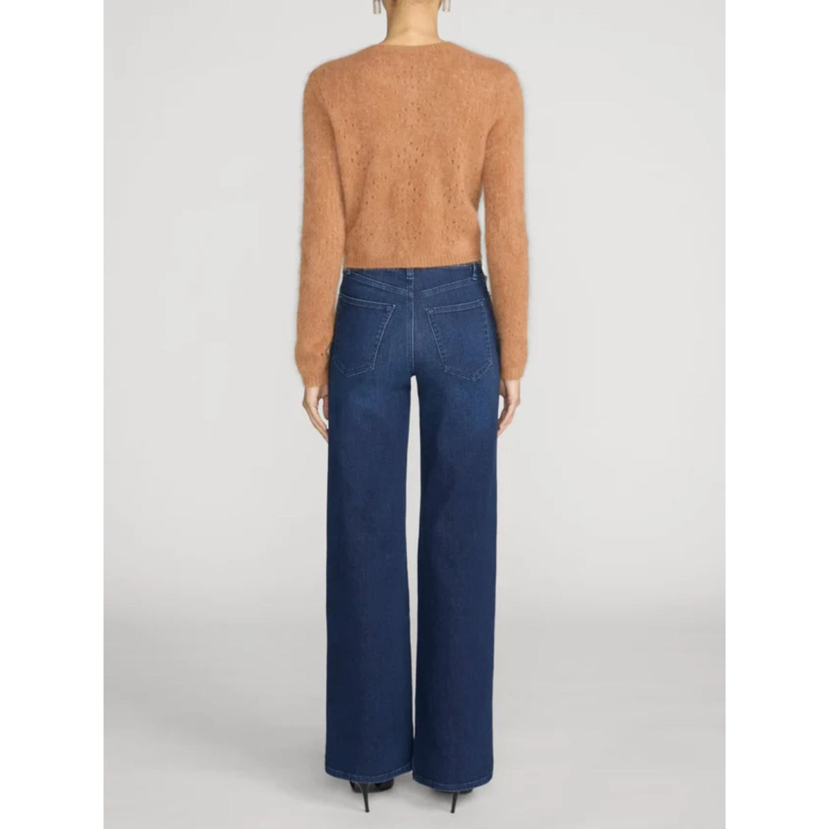 A model shown from the back wearing a fuzzy cropped long-sleeve sweater in a warm camel tan and dark blue wide-leg jeans, set against a plain light gray studio background.