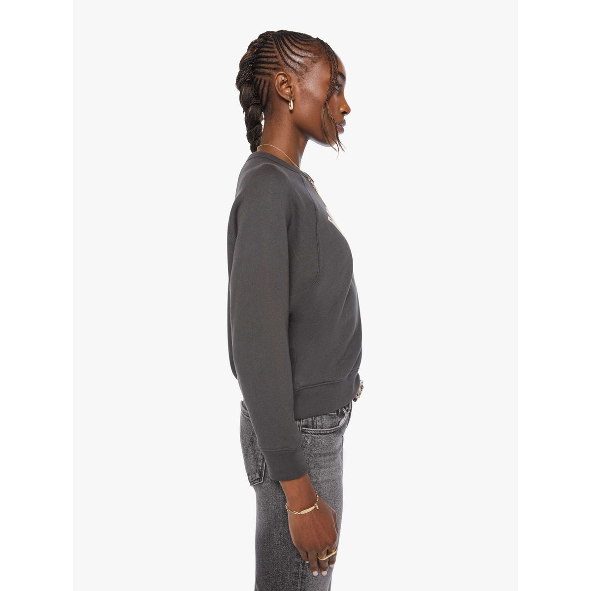 A woman shown in profile wearing a dark charcoal gray crewneck sweatshirt and gray jeans against a plain light gray background.