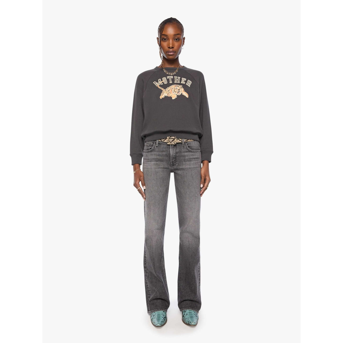 A model stands against a light gray studio background wearing a dark charcoal gray sweatshirt with a beige graphic print that reads 'MOTHER' and 'Gucci', paired with gray jeans and green shoes.