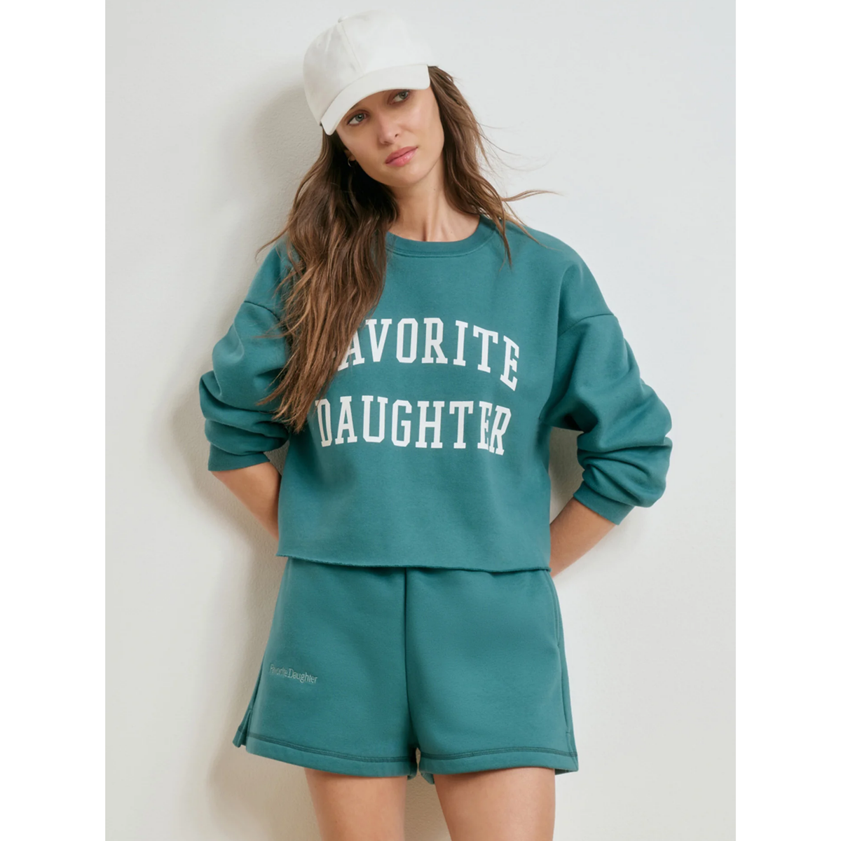 Woman wearing a teal 'FAVORITE DAUGHTER' sweatshirt and shorts set against a white background