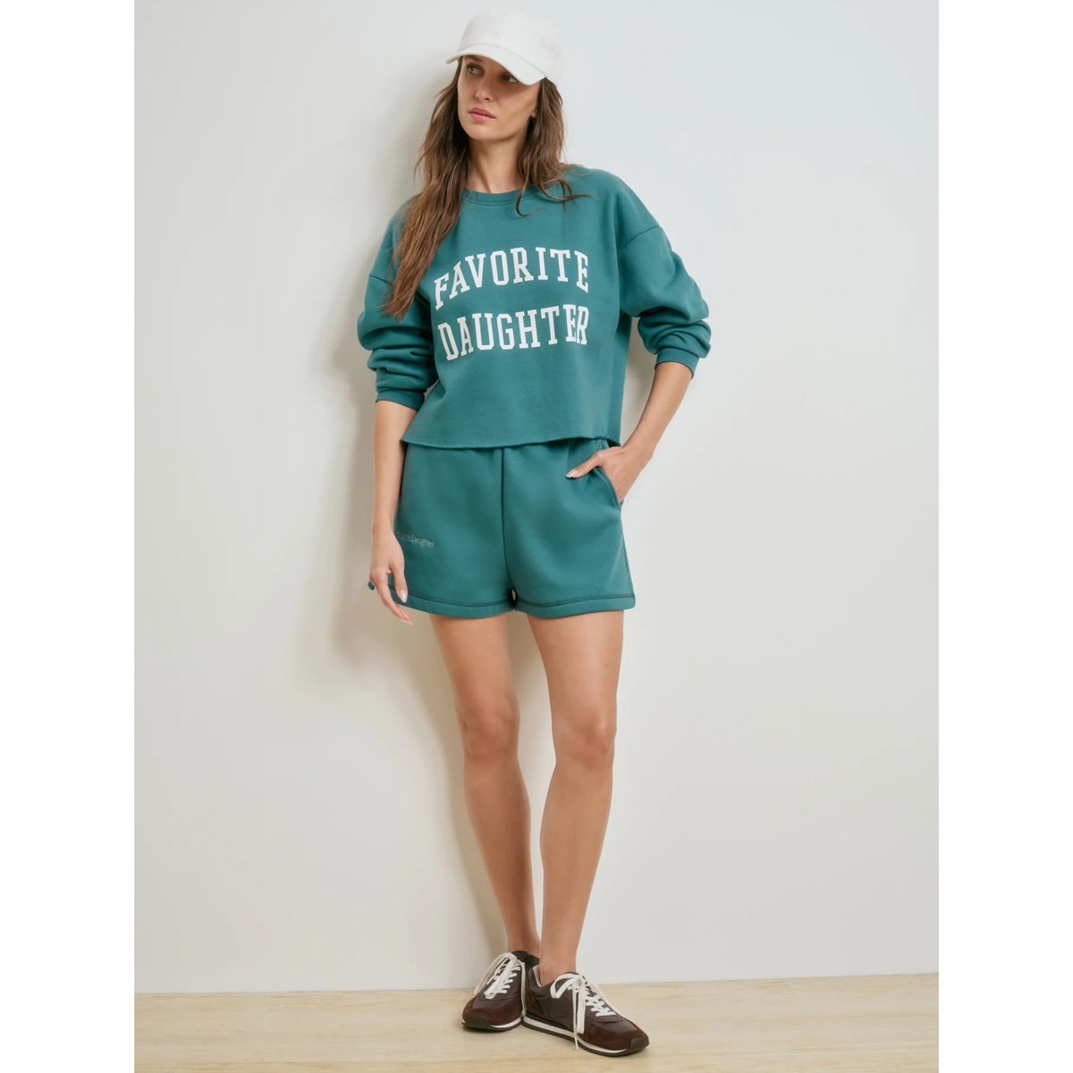 Woman wearing a teal 'Favorite Daughter' sweatshirt and shorts set against a white background