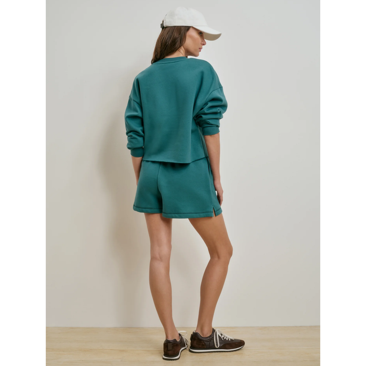Person wearing a teal outfit with shorts and a sweatshirt, standing against a plain background.