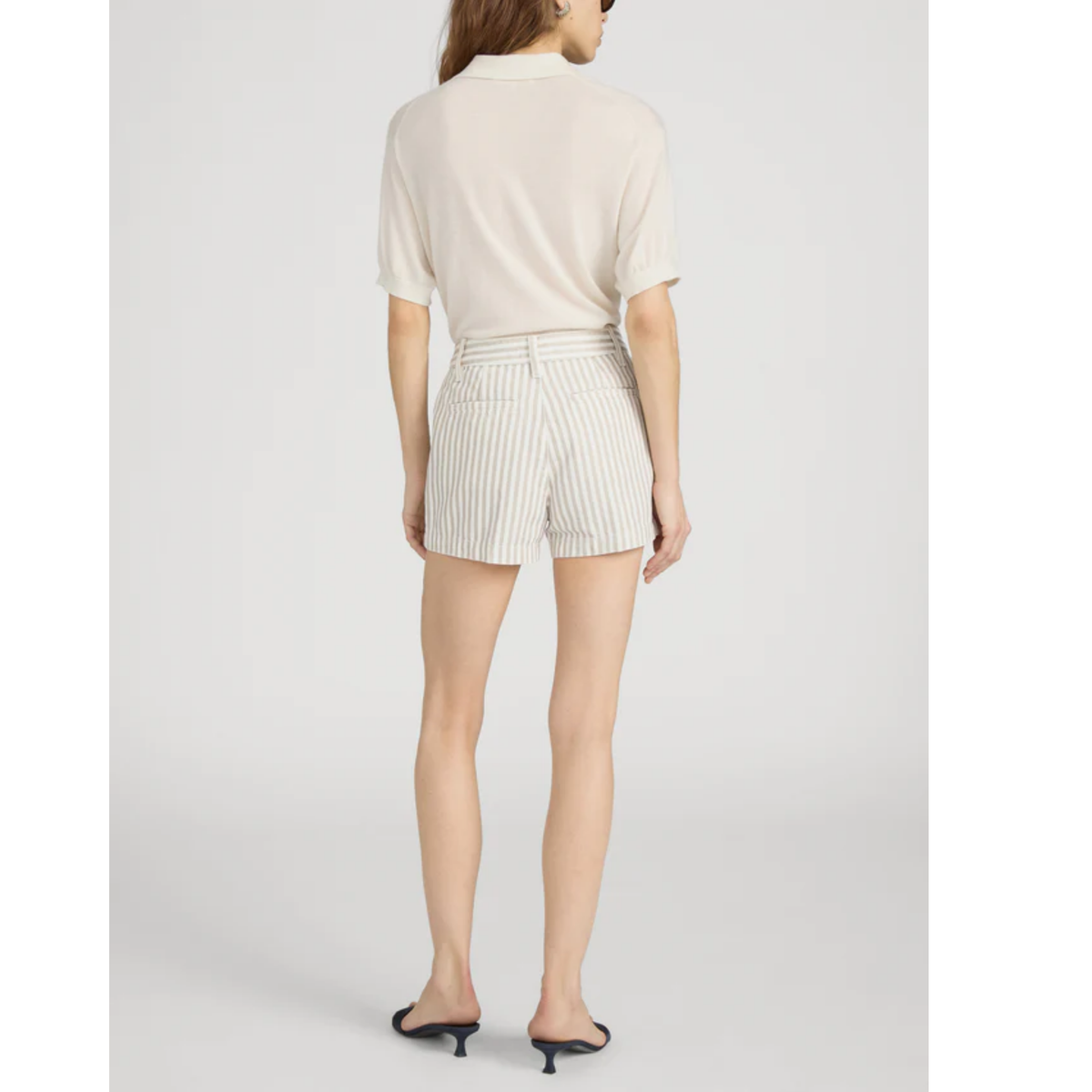 Person wearing a white blouse and striped shorts on a light gray background