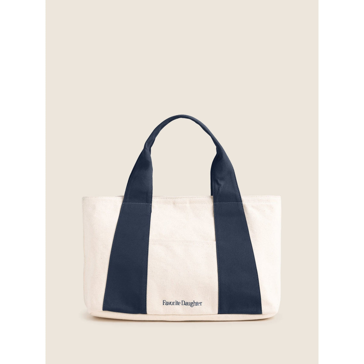 A canvas tote bag with cream-colored body and navy blue handles/panels, featuring the text 'Favorite Daughter' printed on the front, set against a solid light beige background.