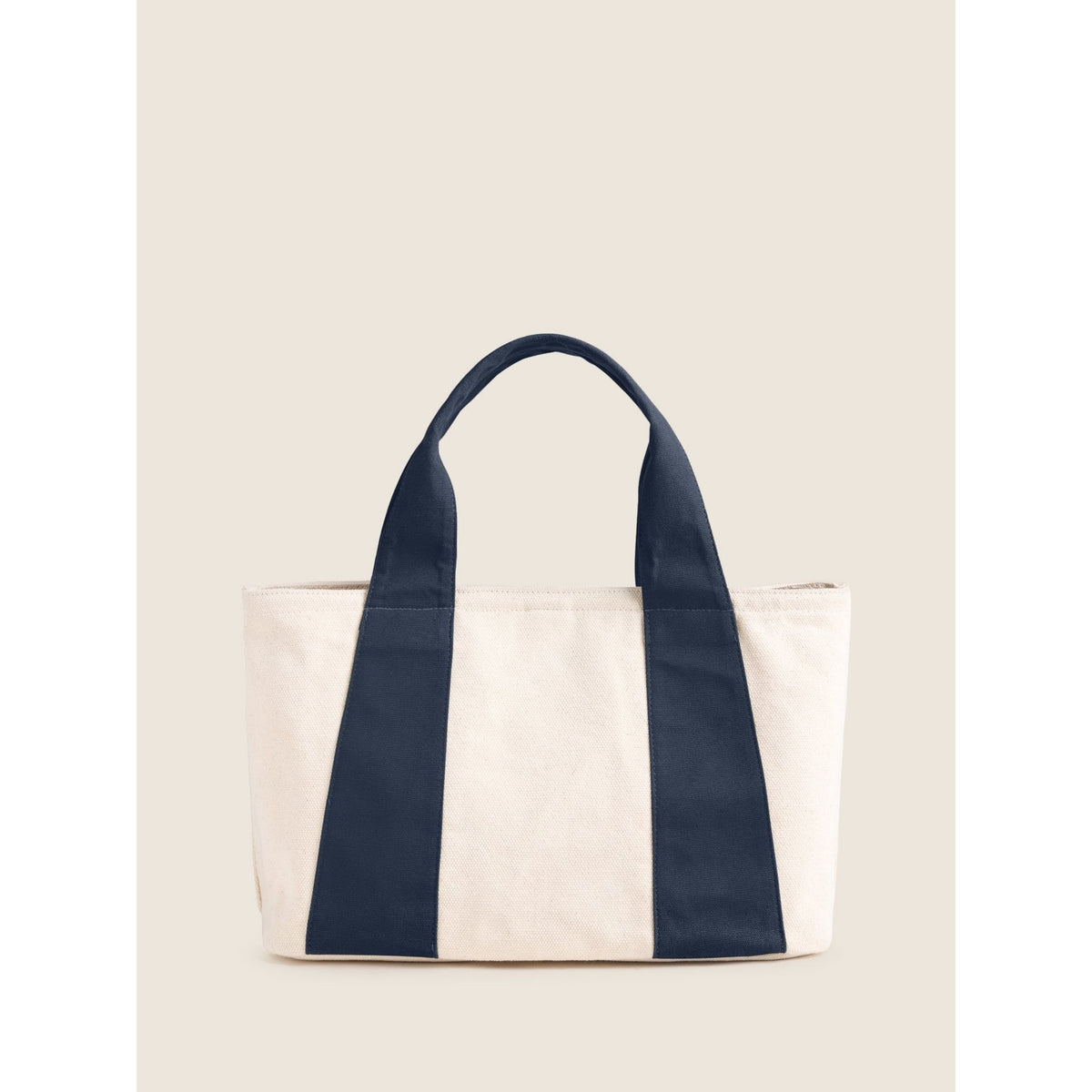 A canvas tote bag with a cream body and dark navy blue vertical side panels and handles, shown against a solid light beige background.