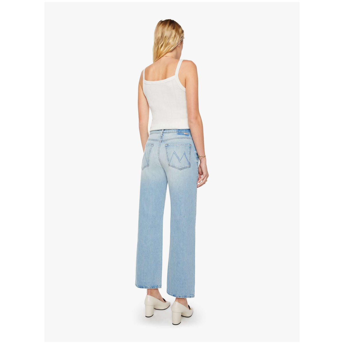 A woman shown from the back wearing light-wash wide-leg denim jeans, a white ribbed tank top, and white heeled shoes against a plain light gray studio background.