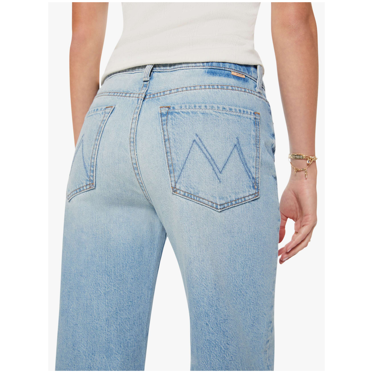 Rear view of a person wearing light-wash blue denim jeans with a white top, shown against a plain light gray background.