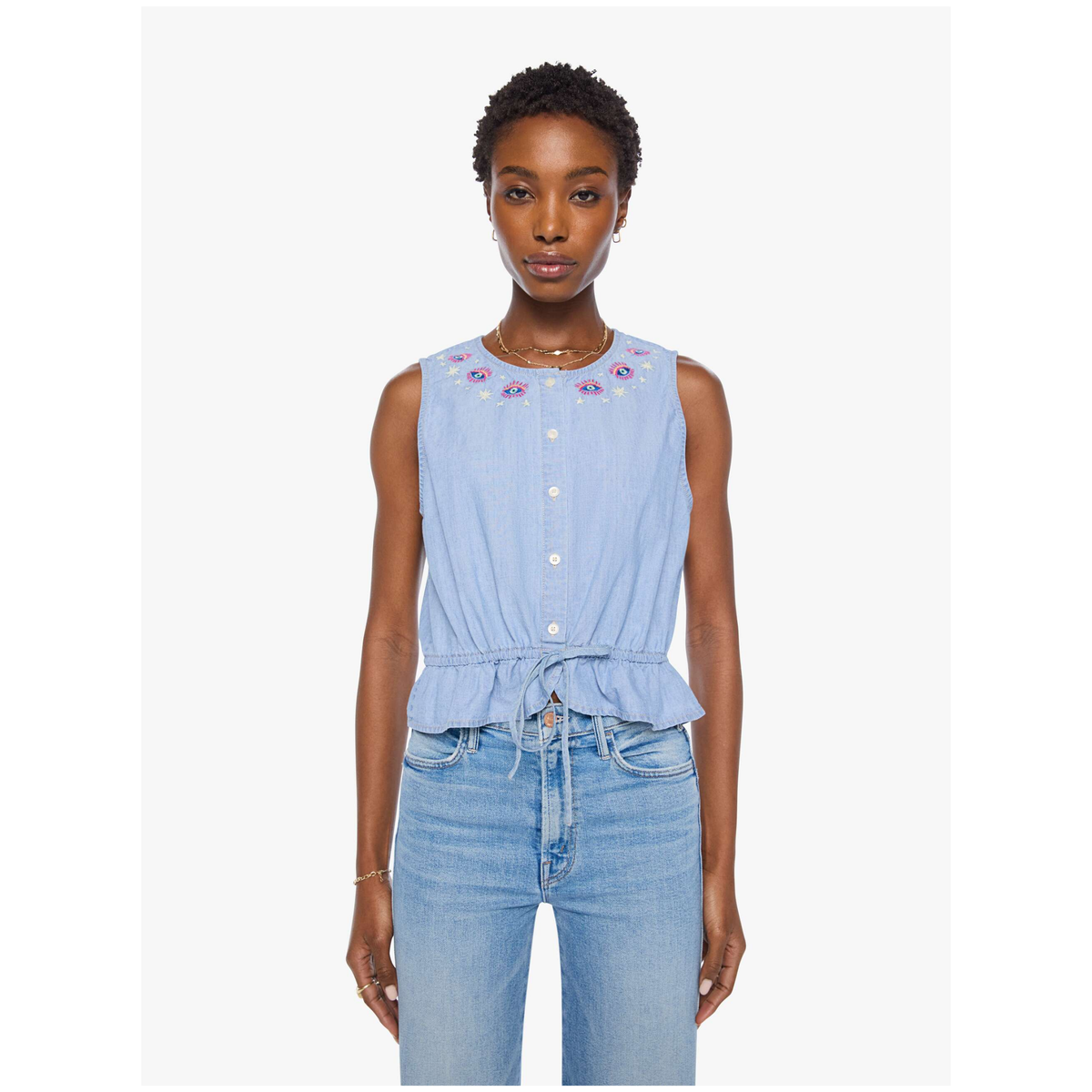 A model wearing a light blue sleeveless button-up top with floral embroidery around the neckline and a tied waist, paired with light blue jeans, against a plain white background.