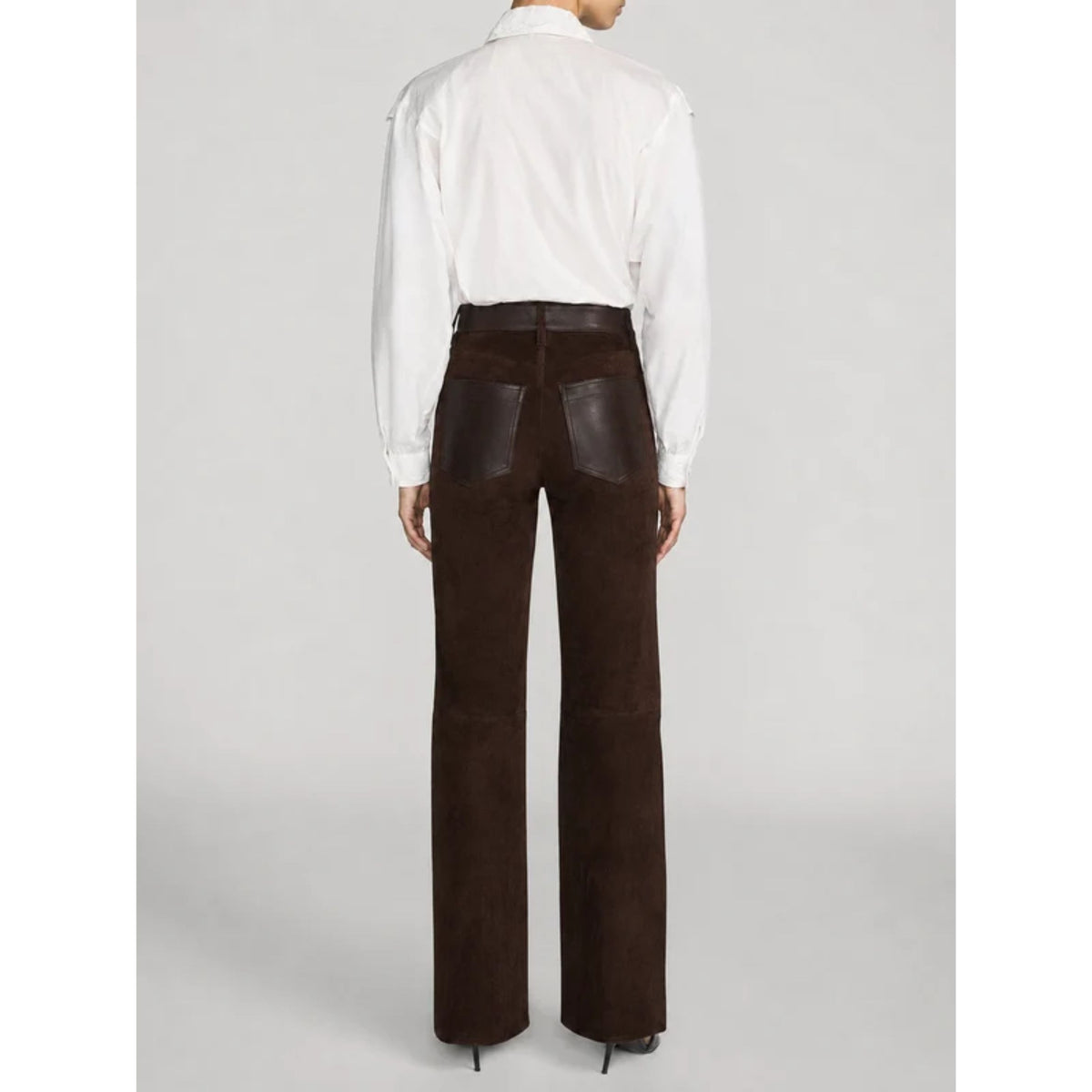 A model shown from the back wearing dark brown wide-leg trousers with dark brown leather patch pockets and a white long-sleeve button-up shirt, set against a light gray studio background.
