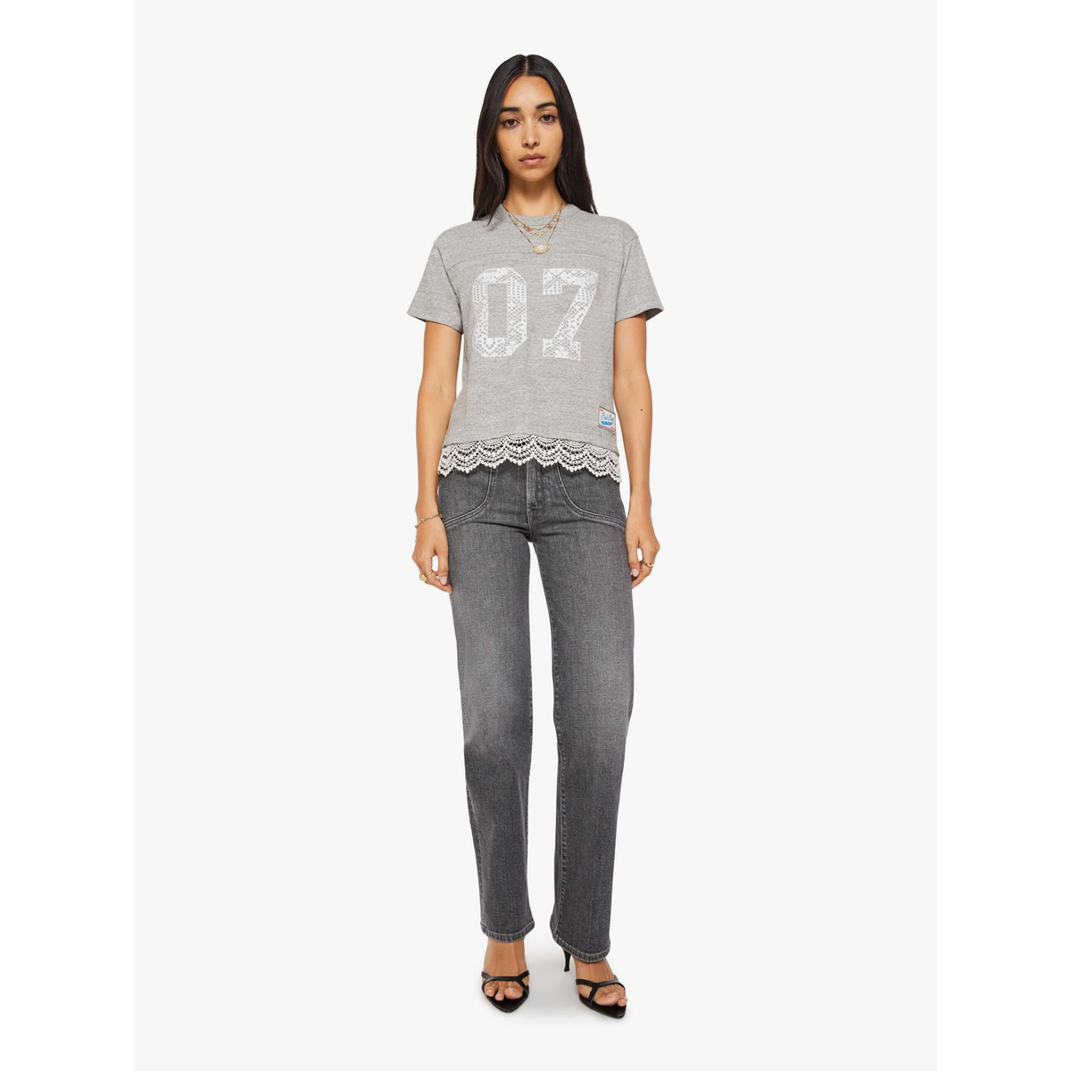 Woman wearing a gray t-shirt with lace trim and gray jeans on a white background
