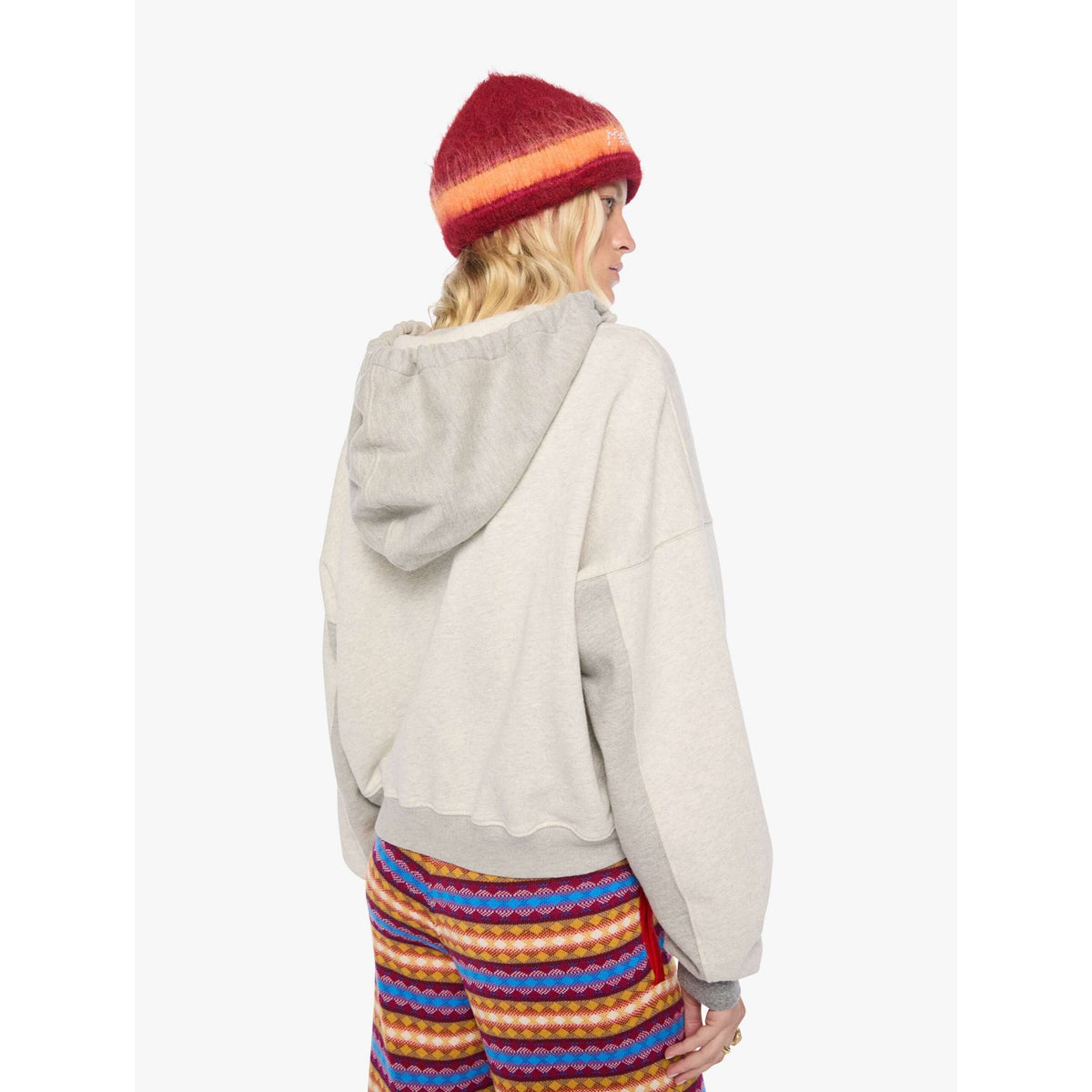 A model shown from the back wearing a light gray oversized hoodie, a red and orange striped knit beanie, and colorful striped pants against a plain white background.