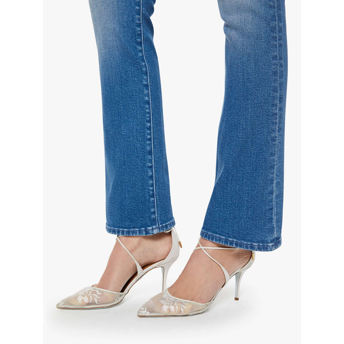 White high-heeled shoes with thin straps worn with blue jeans on a white background