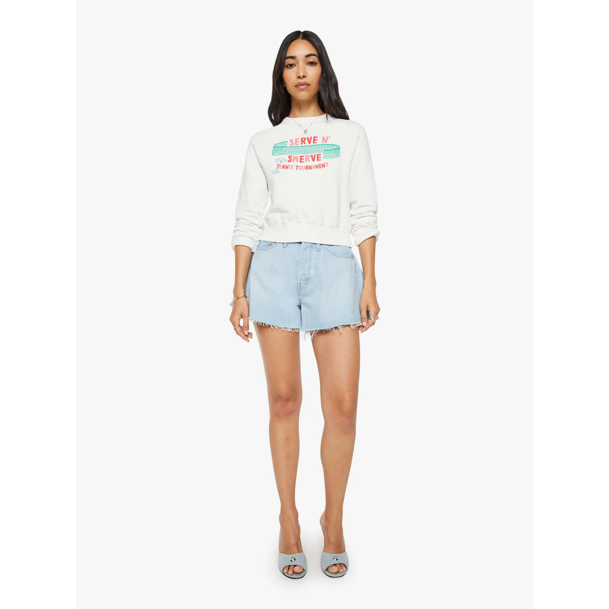 Woman wearing a white sweatshirt with colorful text and light blue denim shorts on a white background