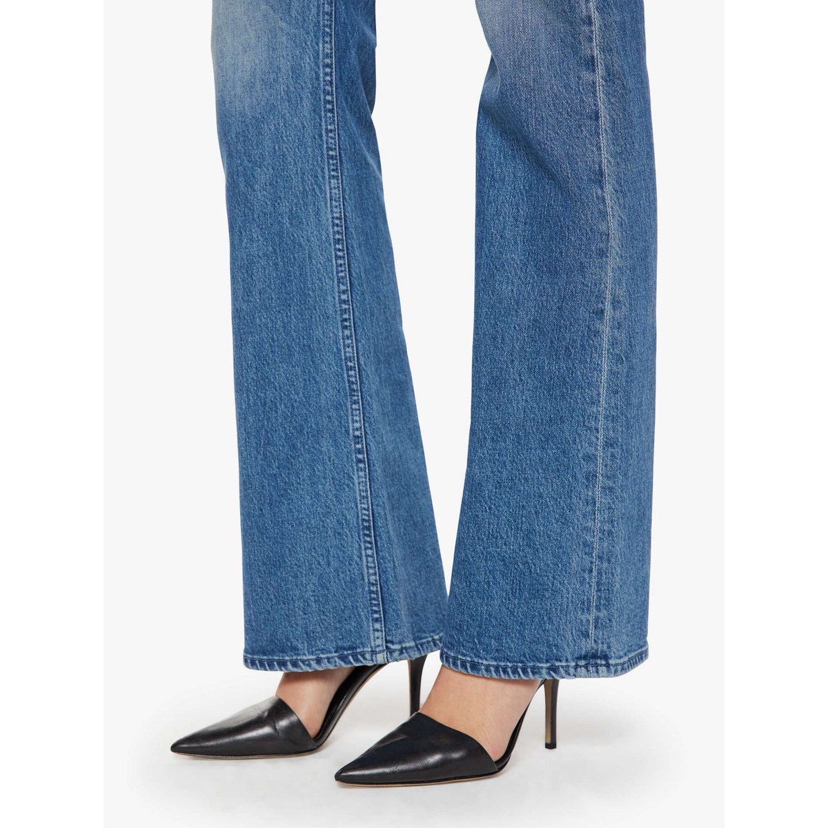 Blue jeans worn with black high-heeled shoes on a white background