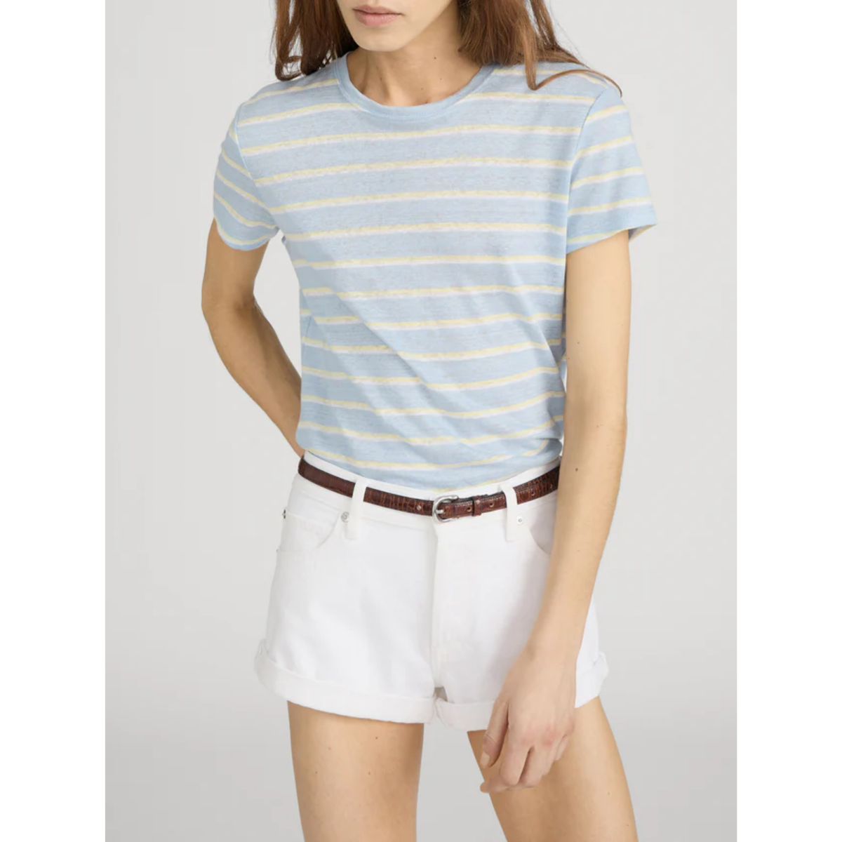 Person wearing a light blue and white striped shirt with white shorts on a plain background