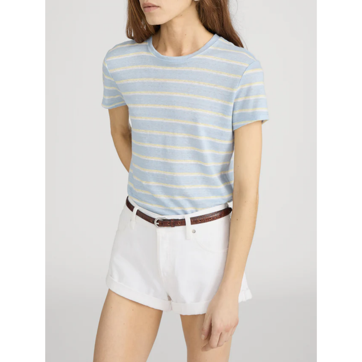 Woman wearing a light blue and white striped shirt with white shorts on a plain background