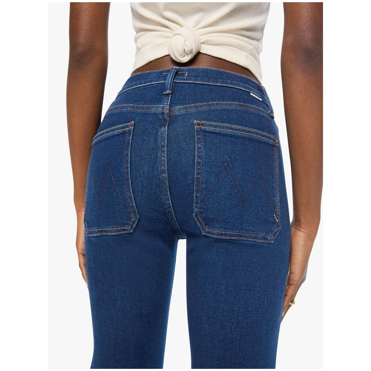 Rear view of a person wearing dark blue denim jeans with a cream knotted crop top, showing the back pockets and waistband details against a light gray background.