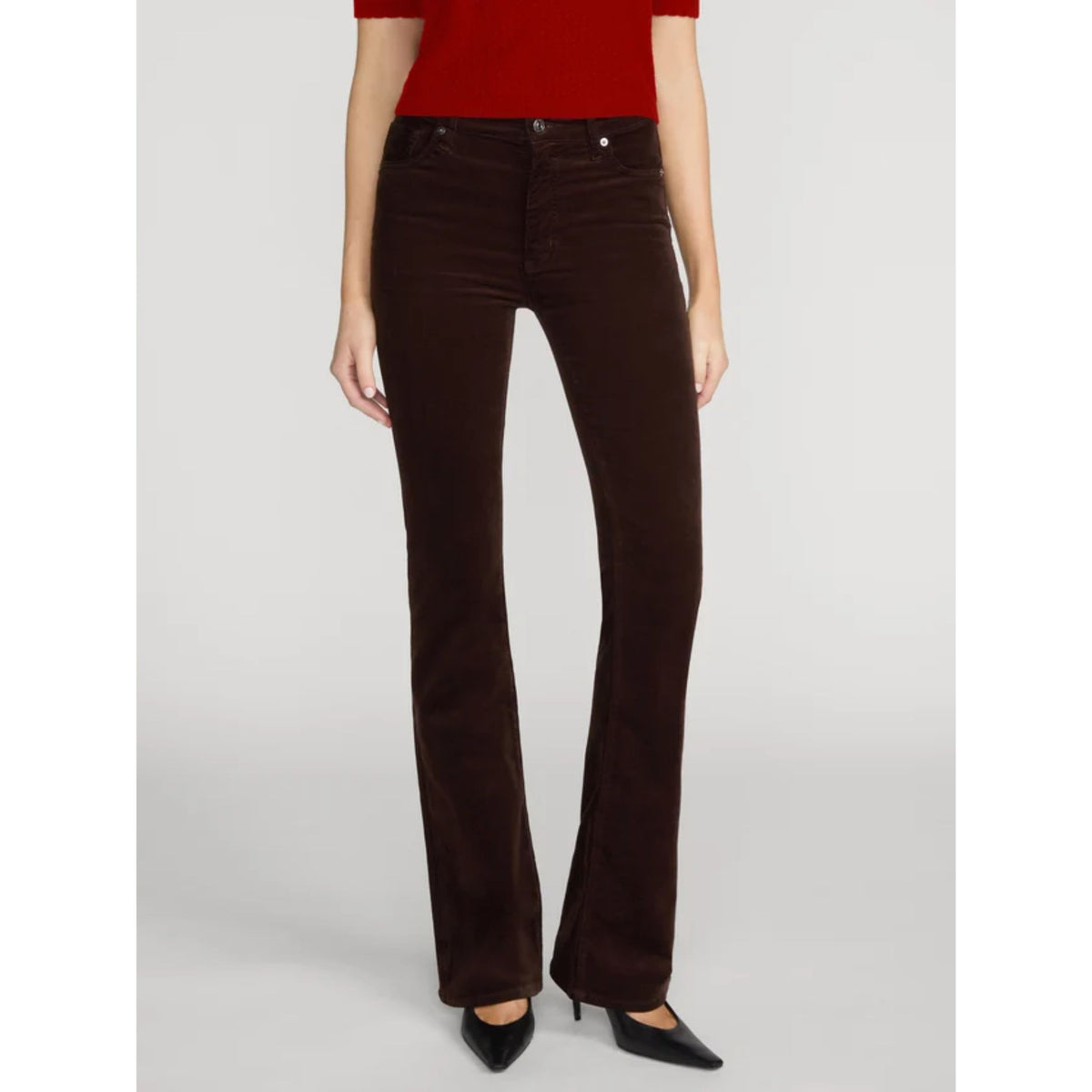 A model wearing dark brown corduroy flare jeans, paired with a red top and black pointed-toe heels, standing against a light gray studio background.