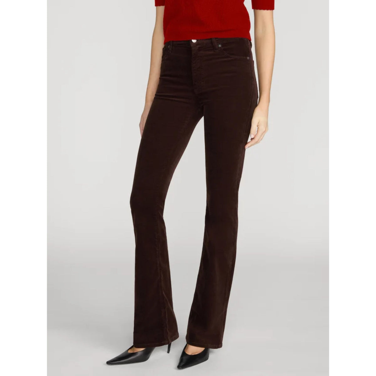 A model wearing dark brown corduroy flare pants with a red top and black pointed-toe heels, shown from the waist down against a light gray studio background.