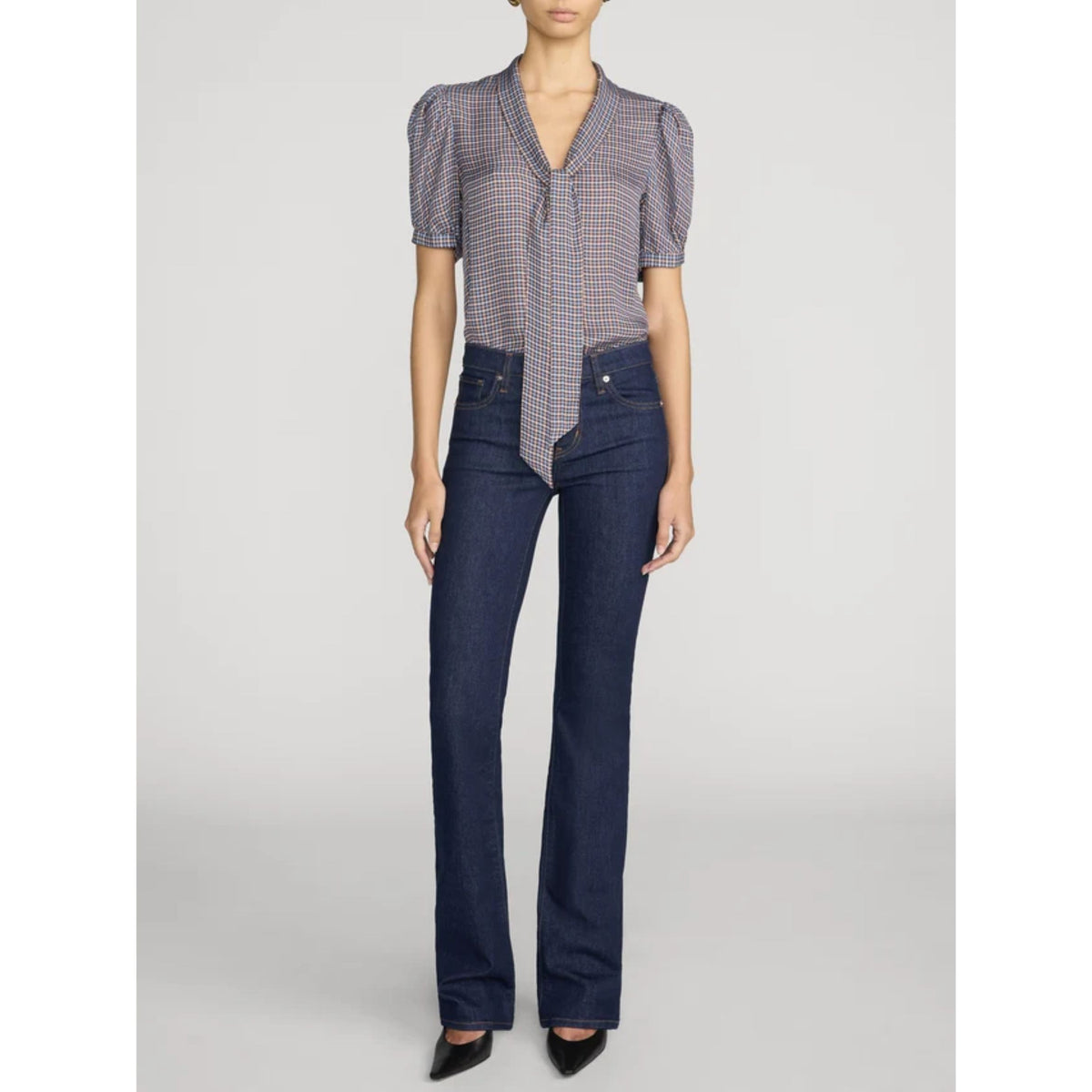 A model wearing a short-sleeve patterned blouse with puffed shoulders and dark blue straight-leg jeans, standing against a light gray studio background.