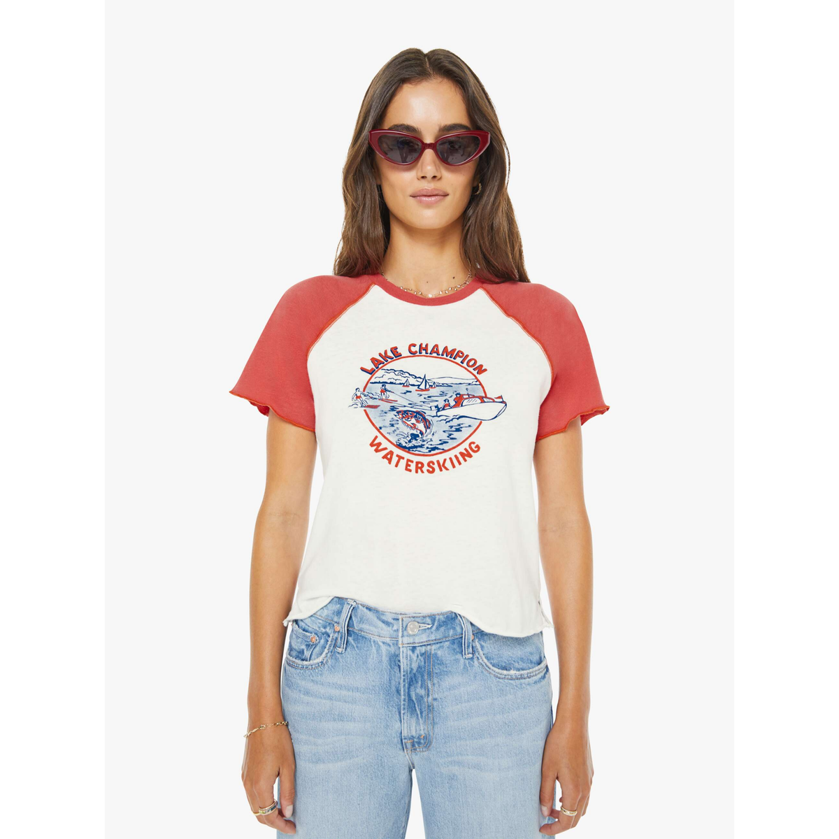 Woman wearing a red and white baseball tee with graphic design and text, standing against a white background.
