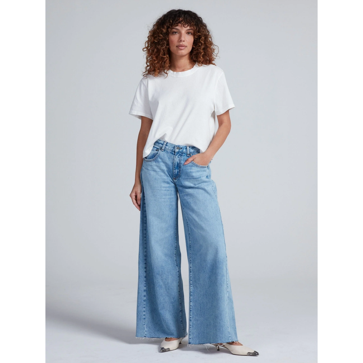 Woman wearing a white t-shirt and light blue jeans on a gray background