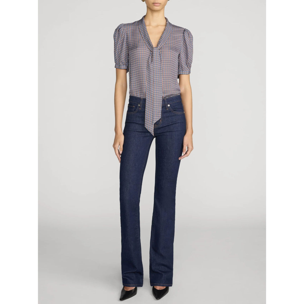 A model wearing a short-sleeve patterned blouse with puffed shoulders and dark blue straight-leg jeans, standing against a light gray studio background.