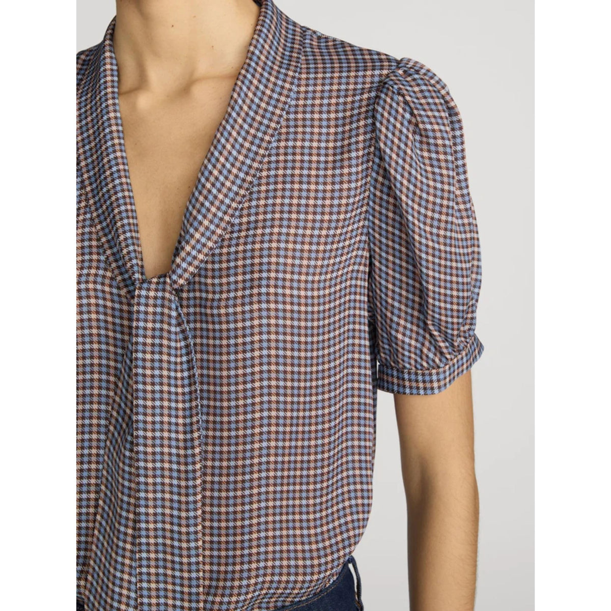 A close-up of a woman wearing a short-sleeve blouse with a blue, red, and white checkered pattern, featuring puff sleeves and a tie-neck detail.