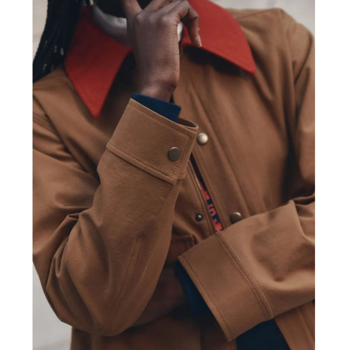 A close-up of a person wearing a brown jacket with a contrasting red collar and a dark blue shirt underneath.