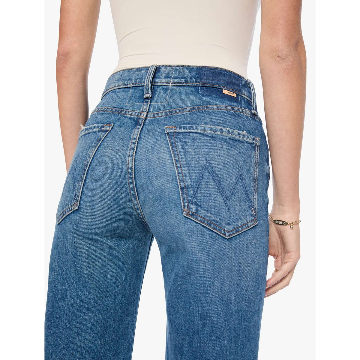 Rear view of a person wearing blue denim jeans with a cream bodysuit, showing the back pockets and waistband details against a plain light background.