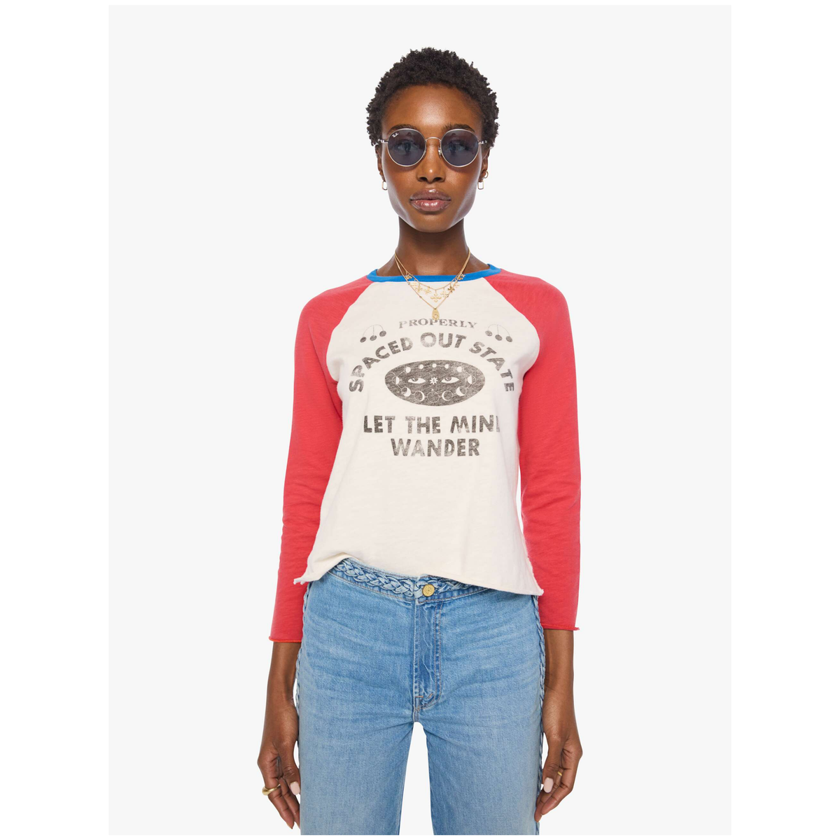 A model wearing a 3/4-sleeve raglan baseball t-shirt with red sleeves, a cream body, and a graphic print that reads 'SPACE OUT STATE LET THE MINI WANDER'. She is also wearing blue jeans and sunglasses, standing against a plain light gray background.