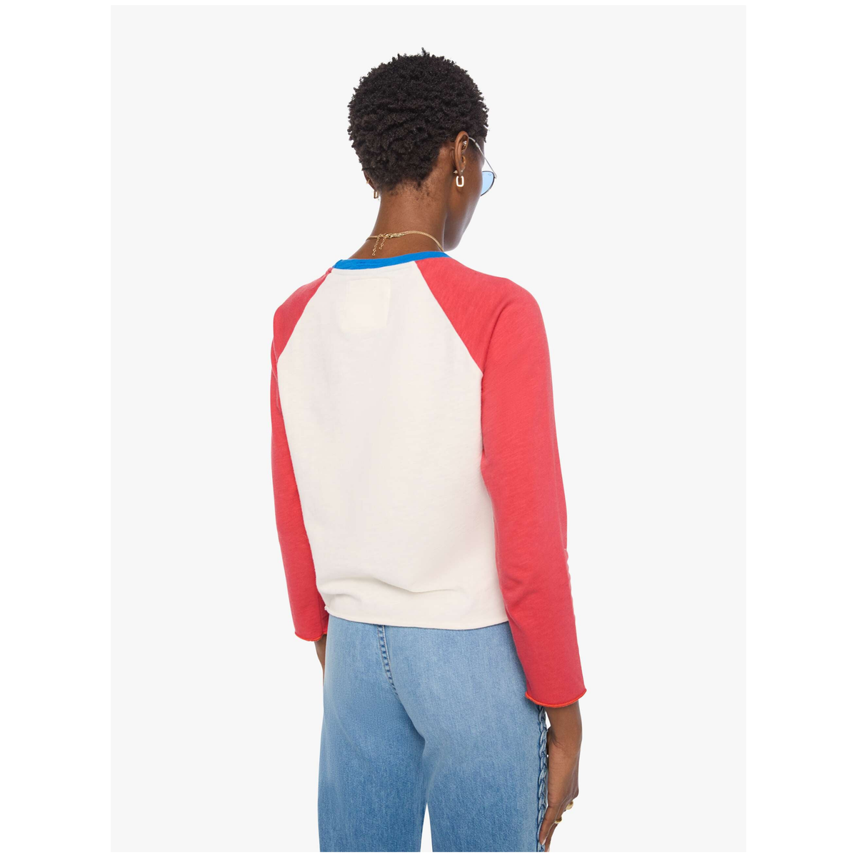 A person shown from the back wearing a colorblock raglan long-sleeve top with an off-white body and red sleeves, featuring a thin blue collar trim, paired with light blue jeans against a light gray background.