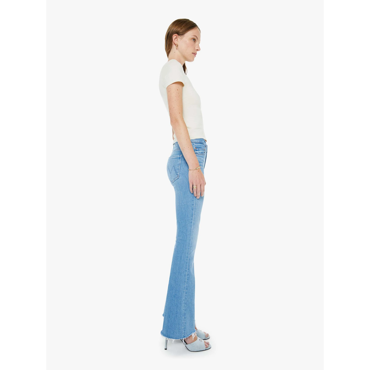 Woman wearing light blue flared jeans and a white top on a white background