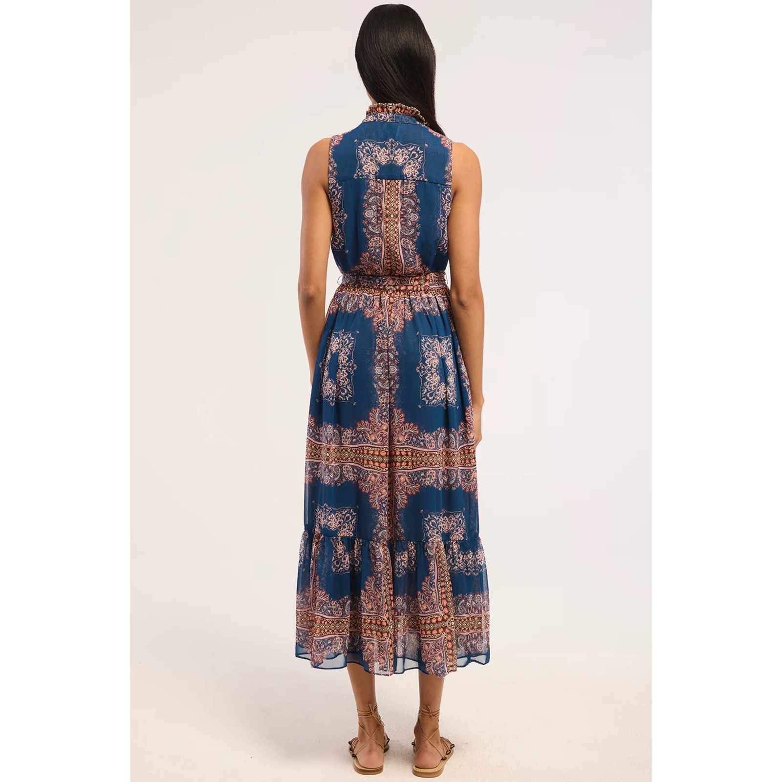 A sleeveless midi dress with a collared neckline, button-front bodice, and self-tie waist belt, featuring a blue base with brown and beige paisley-style patterns, shown against a plain white background.