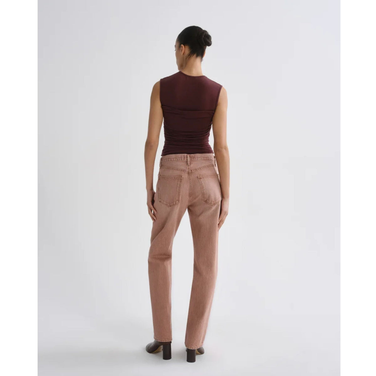 Back view of a model with hair styled in a bun wearing the fitted AGOLDE Theodore Tank in Currant and dusty pink pants against a light gray background.