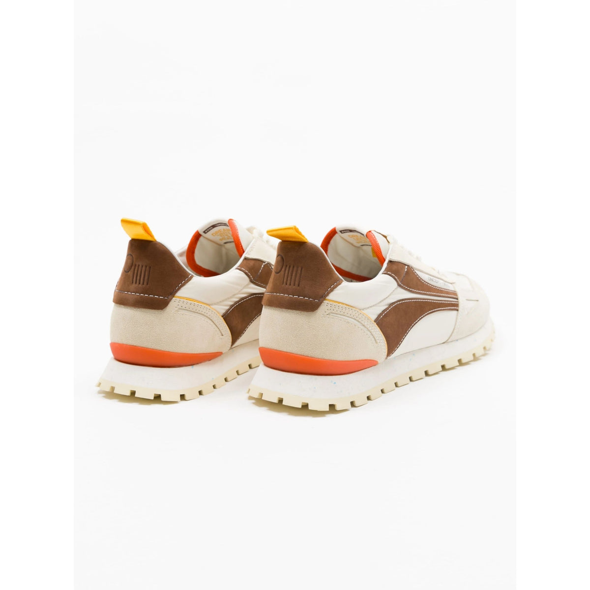 A pair of retro-style low-top sneakers shown from the back, featuring cream and brown suede panels with bright orange accents on the heel, midsole, and pull tabs, set against a plain white background.