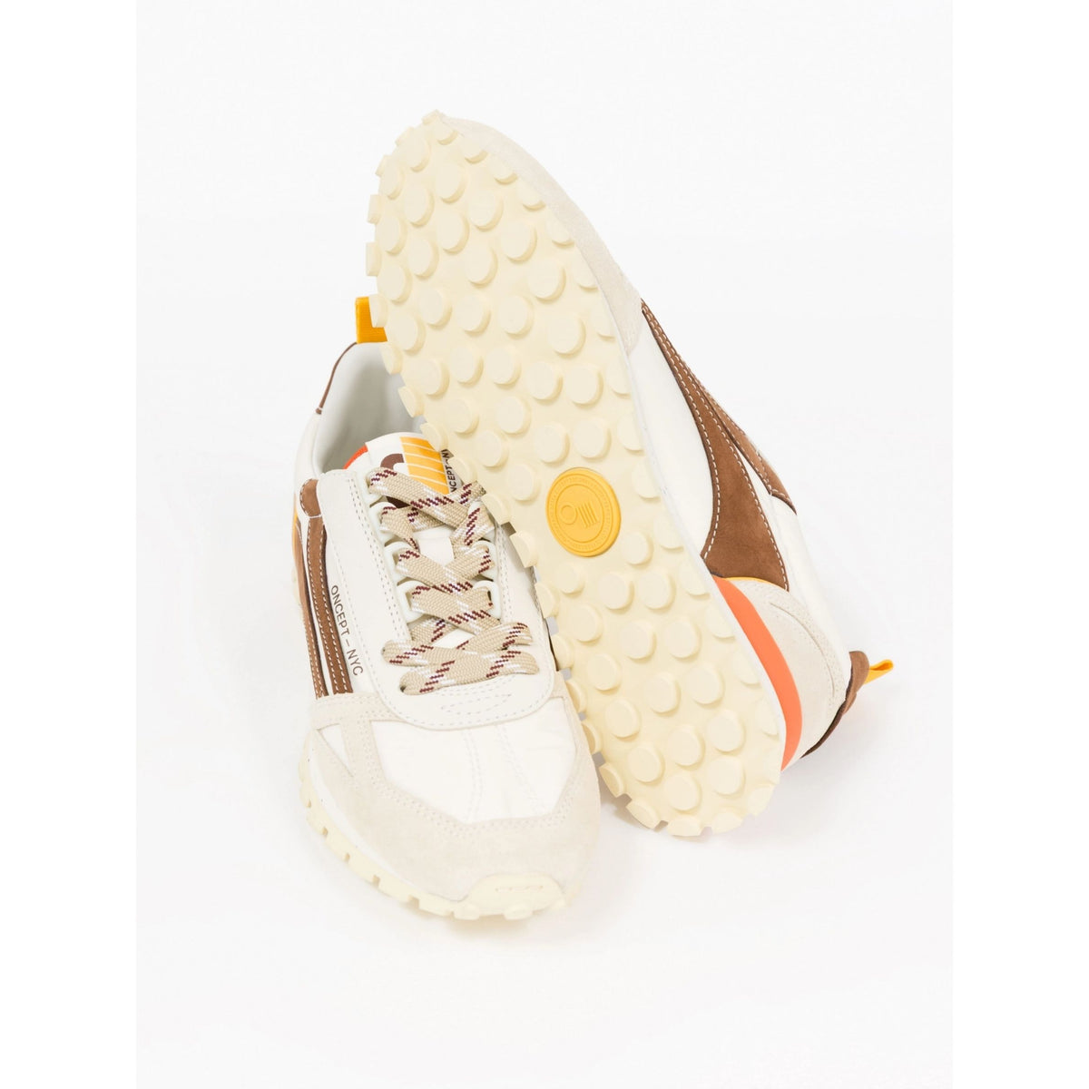 A pair of low-top sneakers shown on a white background, with one shoe standing upright and the other lying on its side to display the textured cream-colored outsole.