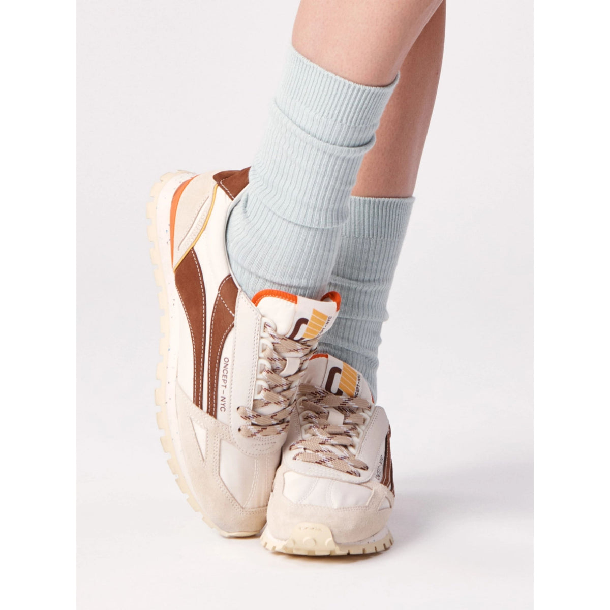 A person wearing cream and brown Reebok sneakers with light blue ribbed crew socks, shown from the knees down against a clean white studio background.