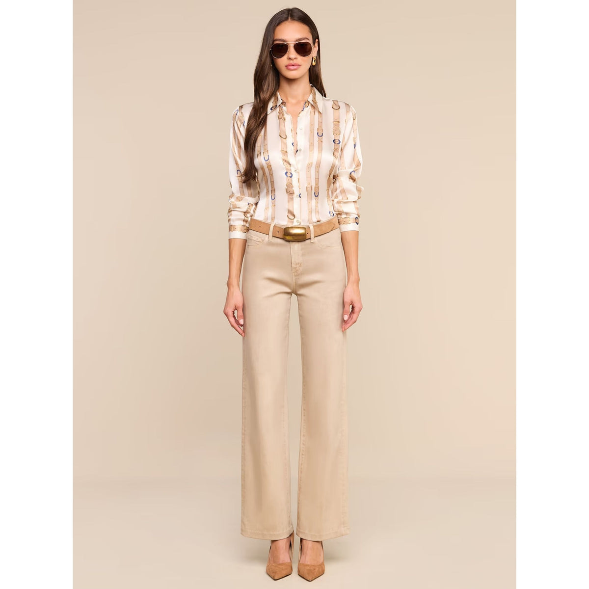 A woman modeling a beige and white striped button-down shirt with a small floral print, paired with beige wide-leg trousers, a tan belt, and tan heels against a solid beige background.