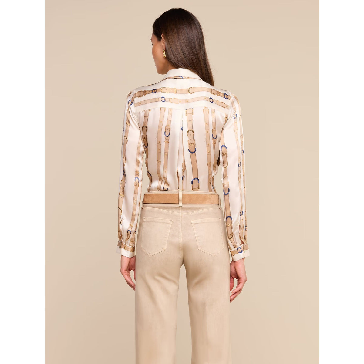 A woman viewed from the back wearing a cream satin shirt with a gold and blue monogram pattern, paired with beige trousers, against a solid beige background.
