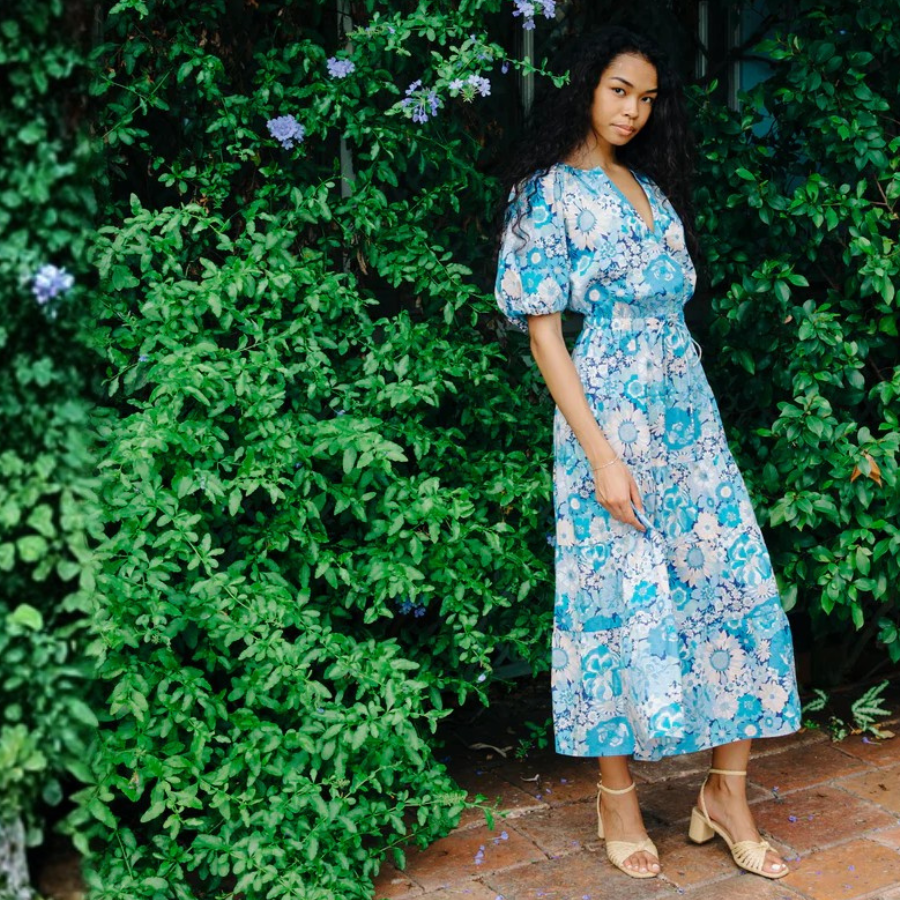 Woman in a blue floral dress standing in front of green foliage