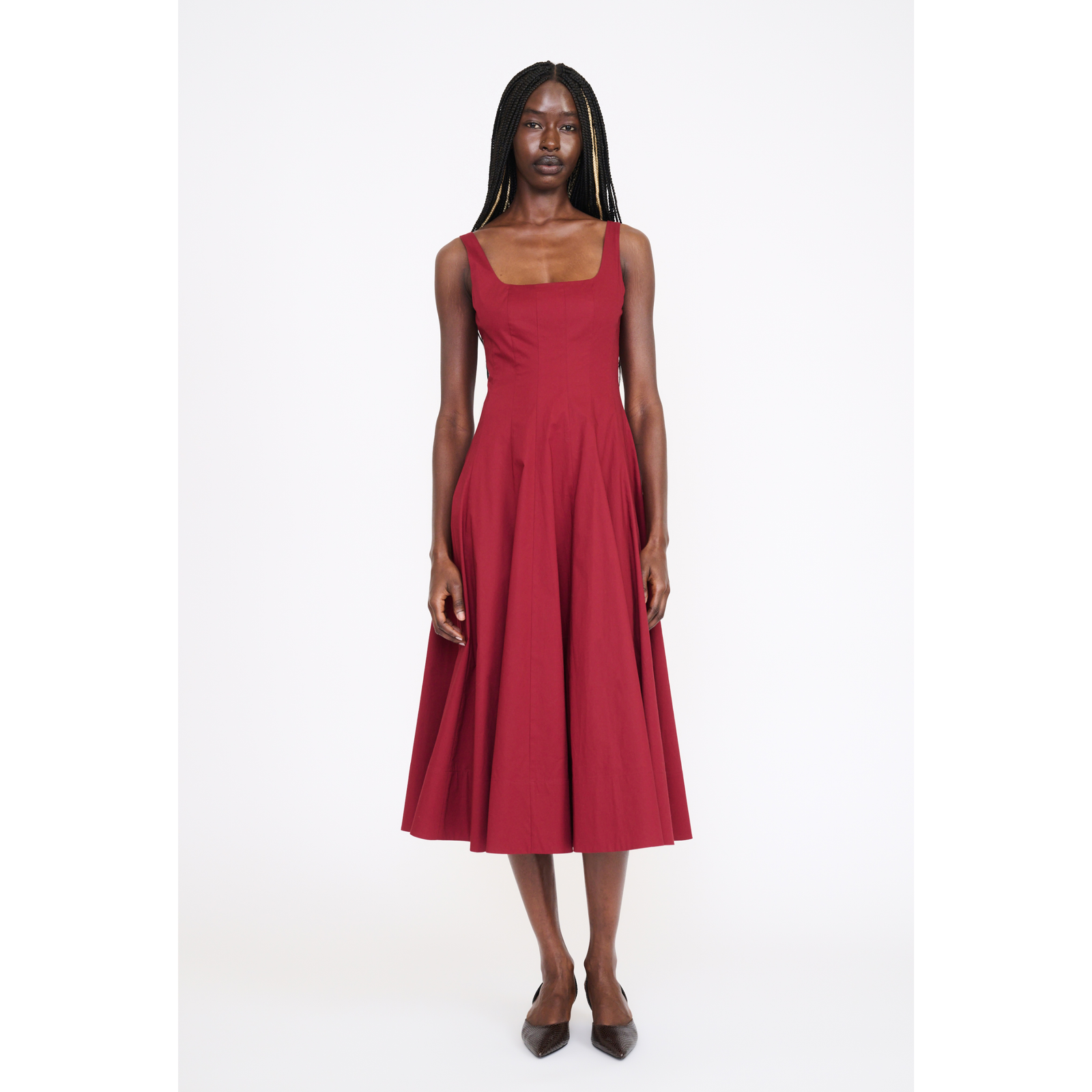 A woman modeling a sleeveless, square-neck midi dress in a deep red or burgundy shade, paired with dark brown pointed-toe heels, against a plain white studio background.