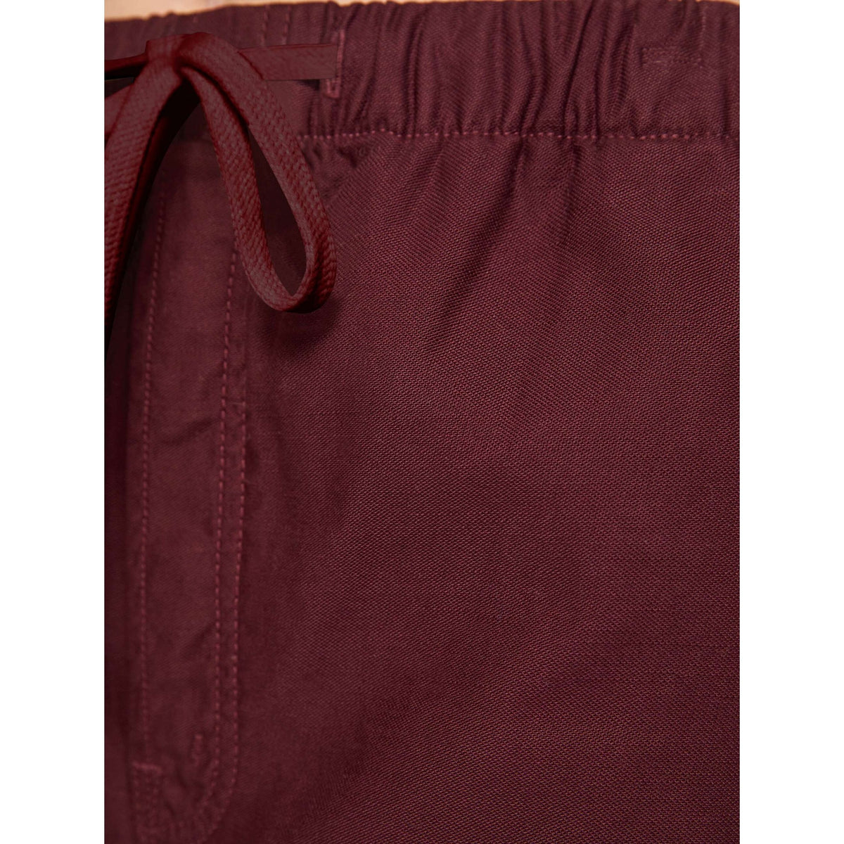 Close-up of burgundy drawstring shorts showing the elastic waistband and fabric texture.